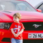 Mustang Auto - Boy Standing in Front of a Red Car