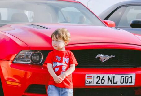 Mustang Auto - Boy Standing in Front of a Red Car